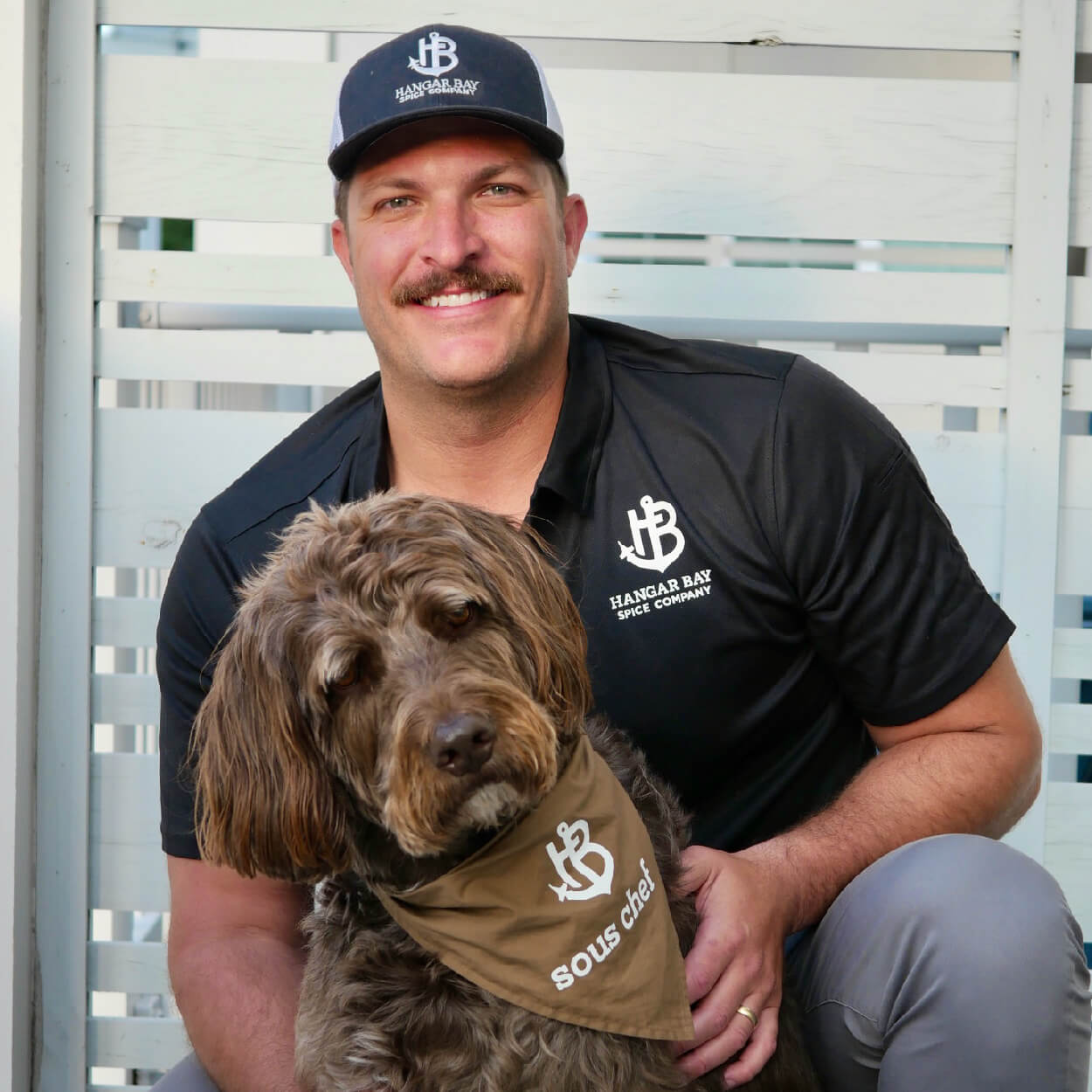 BIFF, Hangar Bay Spice Founder and his dog wearing Hangar Bay merch in front of white fence