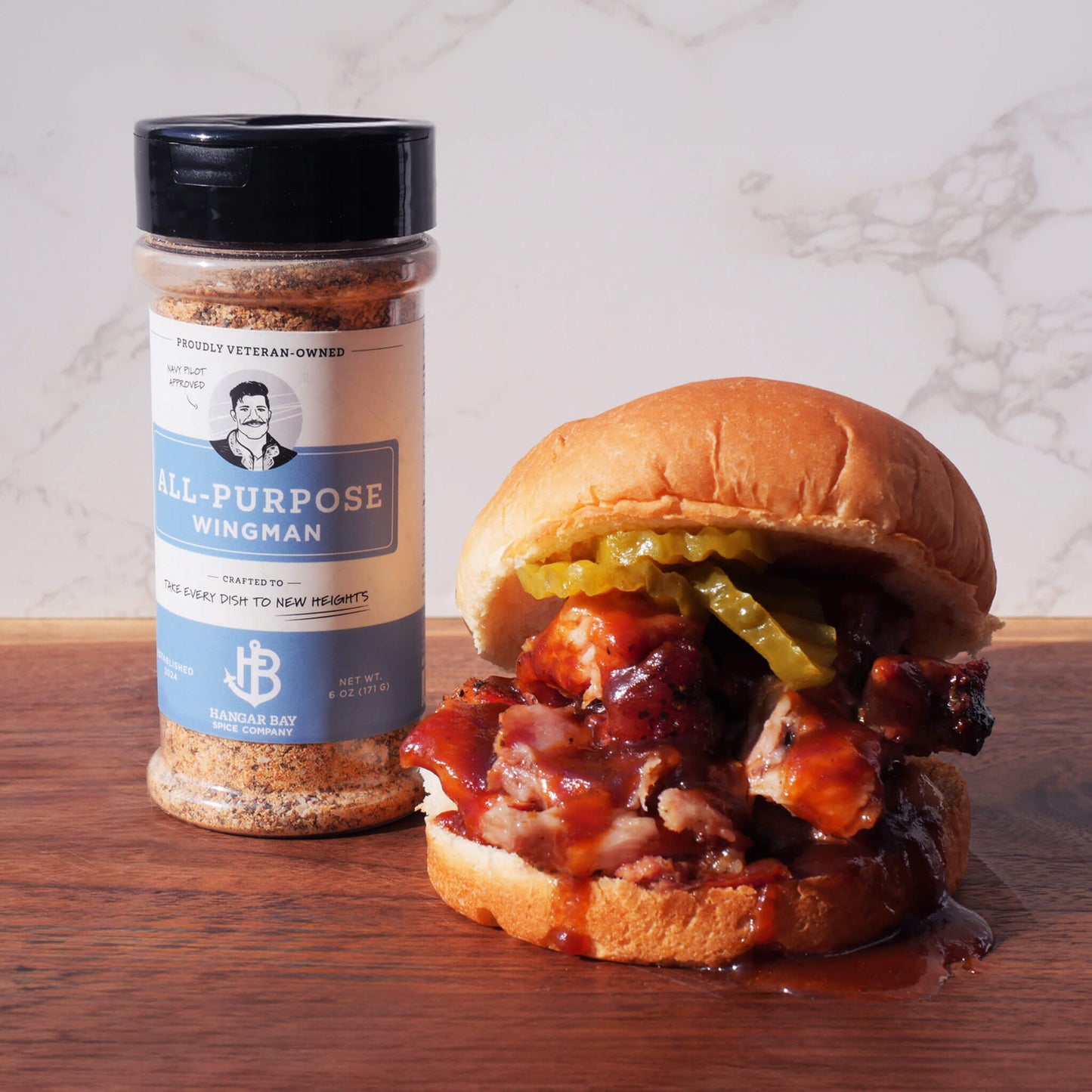 Wingman All-Purpose Seasoning with brisket sandwich on hamburger bun with sauce and pickles